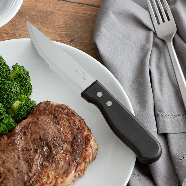 A white plate with a Choice steak knife next to a steak and broccoli.