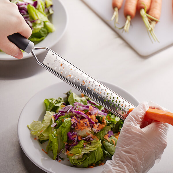 A person using a Mercer Culinary Coarse Grater to grate a carrot.