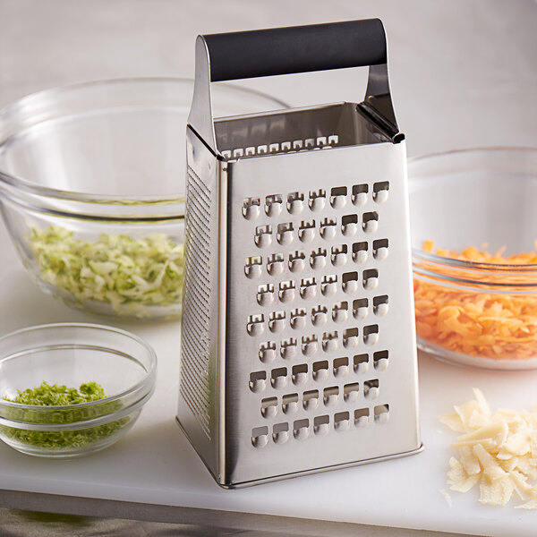 A Mercer Culinary stainless steel box grater with a black handle and a variety of vegetables on it.