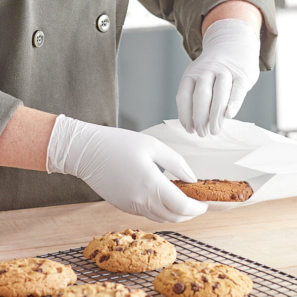 A person wearing Noble Products blue nitrile gloves holding a cookie.