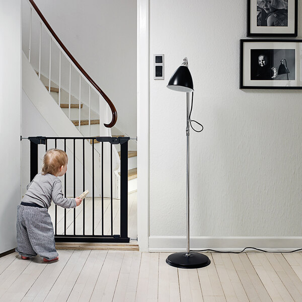 A baby standing by a L.A. Baby black pressure mount safety gate.