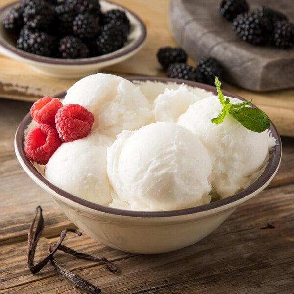 A Carlisle sweet cream melamine ice cream bowl filled with white ice cream and raspberries.