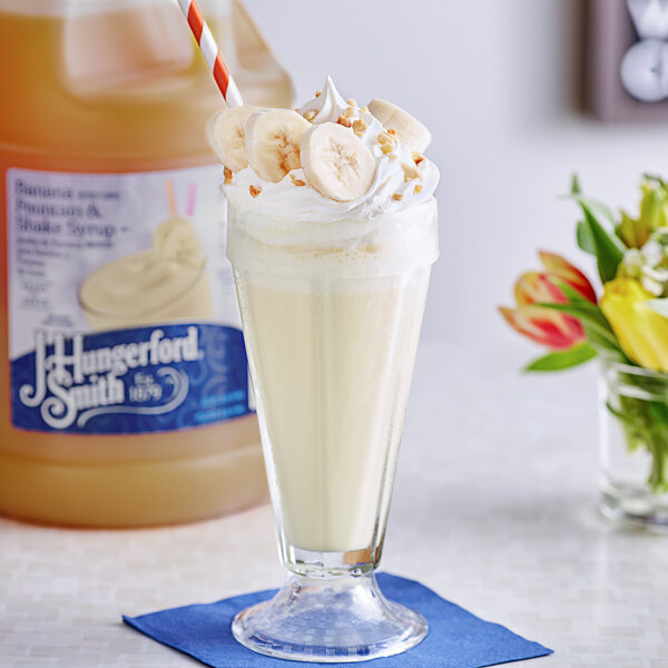 A bottle of J. Hungerford Smith Banana Syrup with a glass of milkshake topped with whipped cream and a banana slice.