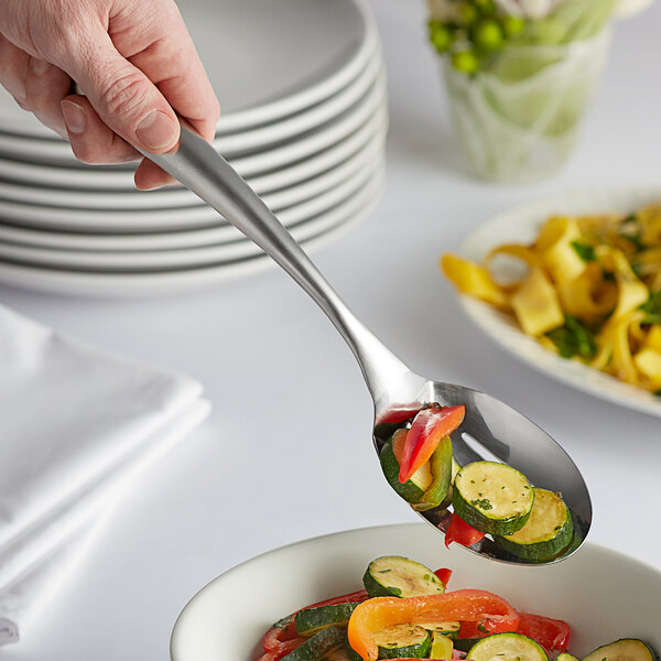 A hand using a Tablecraft Dalton II slotted serving spoon to serve vegetables.