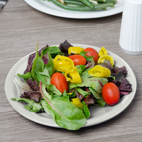 A Carlisle bone melamine salad plate with lettuce, tomatoes, and peppers.