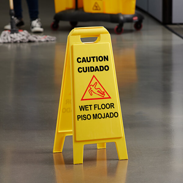 A yellow Carlisle wet floor sign with "Caution Wet Floor" in English and Spanish on the floor.