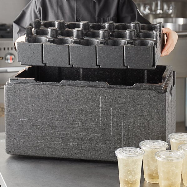 A person holding a Cambro black top loading EPP food pan carrier with a stack of plastic cups.