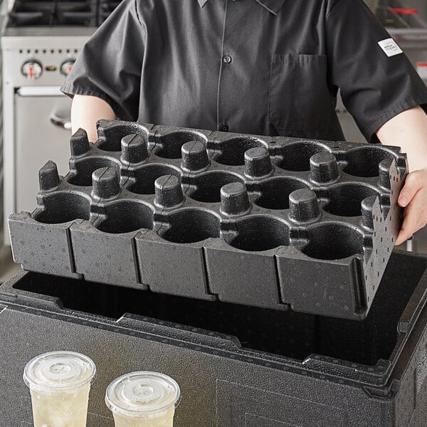 A woman holding a black Cambro container with cups in a tray.