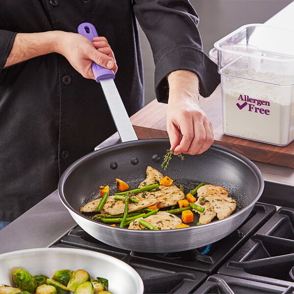 A person using a Choice aluminum frying pan with a purple handle to cook food.