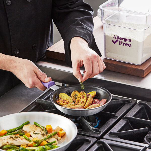 A person using a Choice 7" aluminum non-stick fry pan with a purple allergen-free silicone handle to cook food on a stove top.