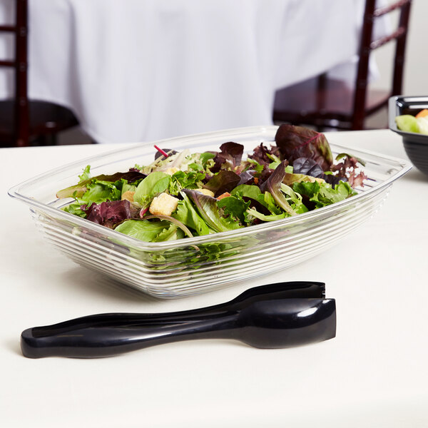 A salad in a Cambro clear rectangular ribbed bowl on a table.