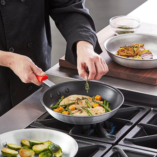 A person cooking food in a Choice aluminum non-stick fry pan.