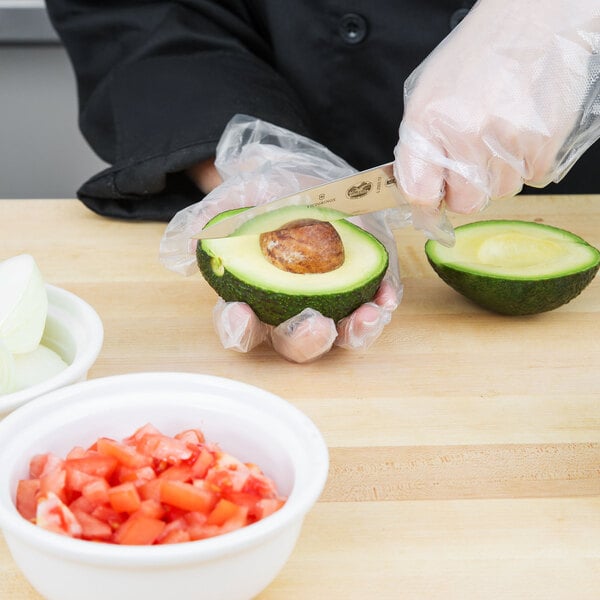 A person using a Victorinox chef knife to slice an avocado on a counter.
