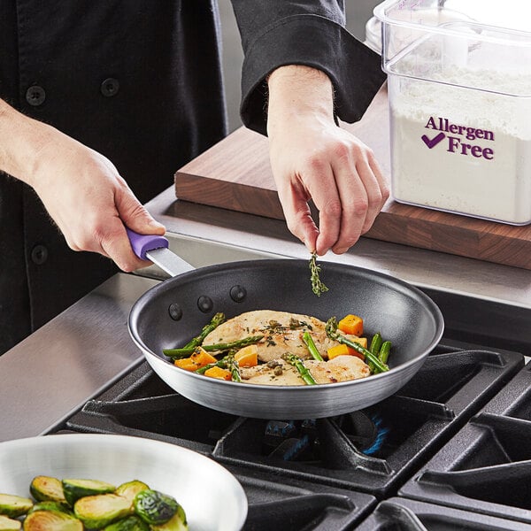 A person cooking food in a Choice purple aluminum non-stick fry pan with a purple handle.