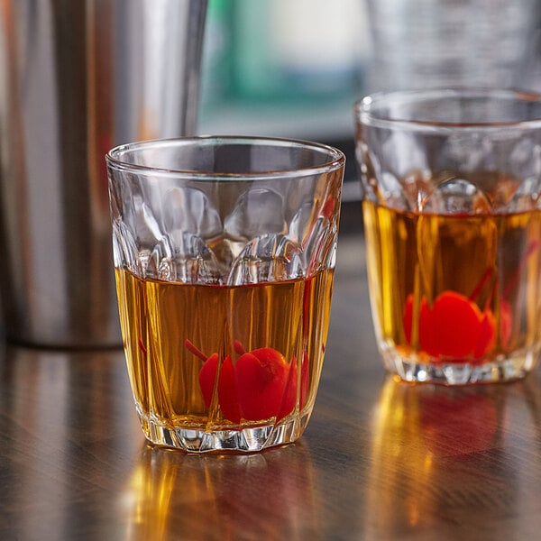 Two Duralex glass tumblers filled with liquid and cherries on a table.