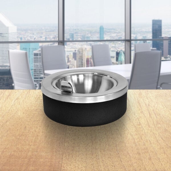 An Ex-Cell Kaiser black and stainless steel tabletop ashtray with a flip top on a table.