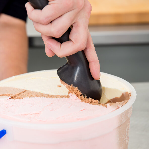 A hand using a Zeroll ice cream scoop to scoop pink and white ice cream.