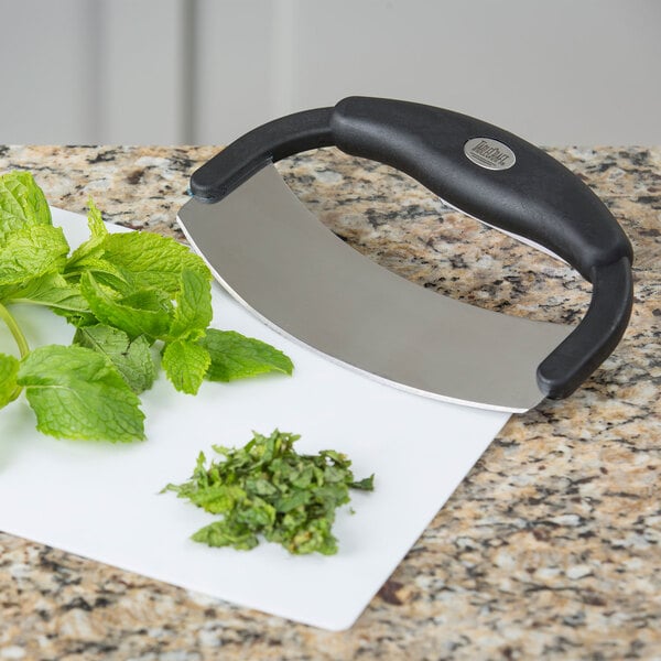 A Tablecraft single blade mezzaluna knife with a silicone handle on a cutting board with mint leaves.