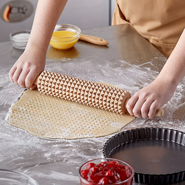 A person rolling out pizza dough on a table with a Linden Sweden beech wood deep notch rolling pin.