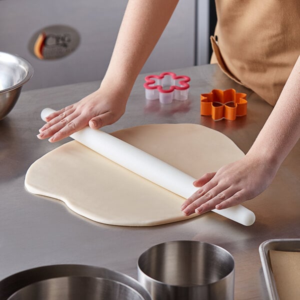 A person using an Ateco Tapered French Rolling Pin to roll out dough on a counter.