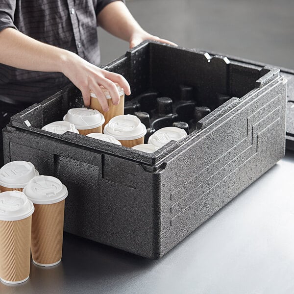 A woman putting coffee cups in a black Cambro food pan carrier.