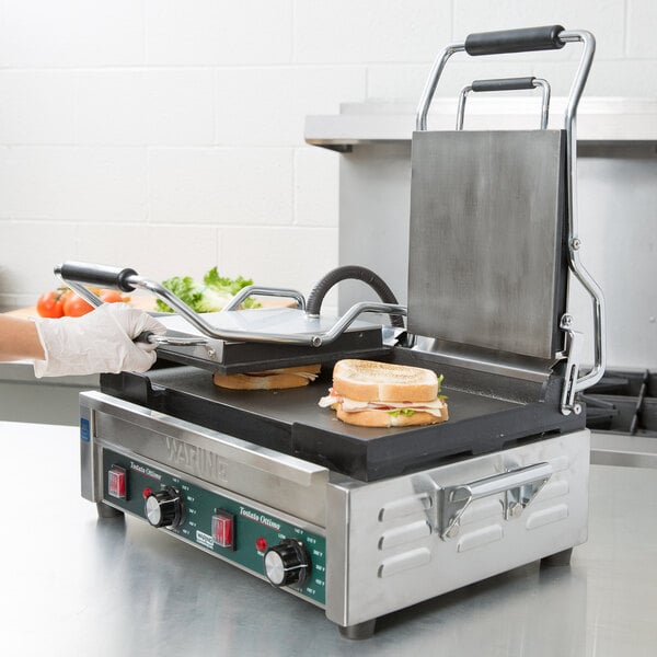 A person using a Waring Tostato Ottimo Panini Grill to make a sandwich with meat and lettuce.