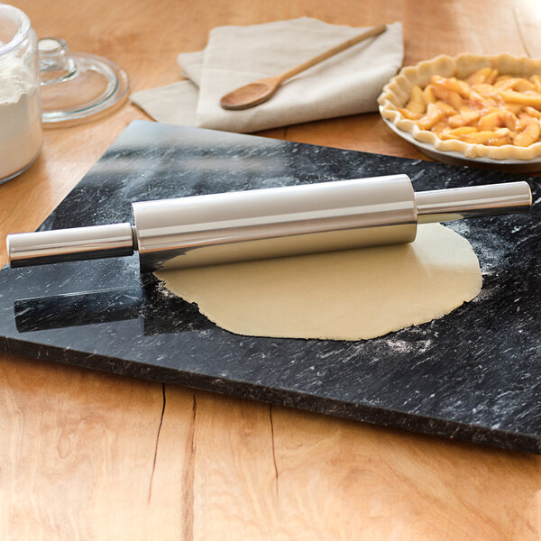 A Fox Run stainless steel rolling pin on a black board with a pie and a bowl of macaroni.