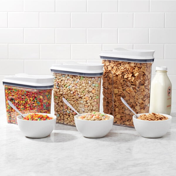 A clear OXO rectangular plastic food storage container filled with cereal next to a bottle of milk.