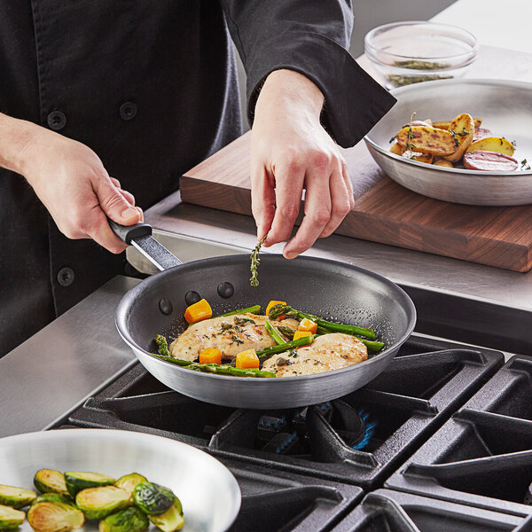 A person cooking food in a Vollrath aluminum non-stick fry pan.