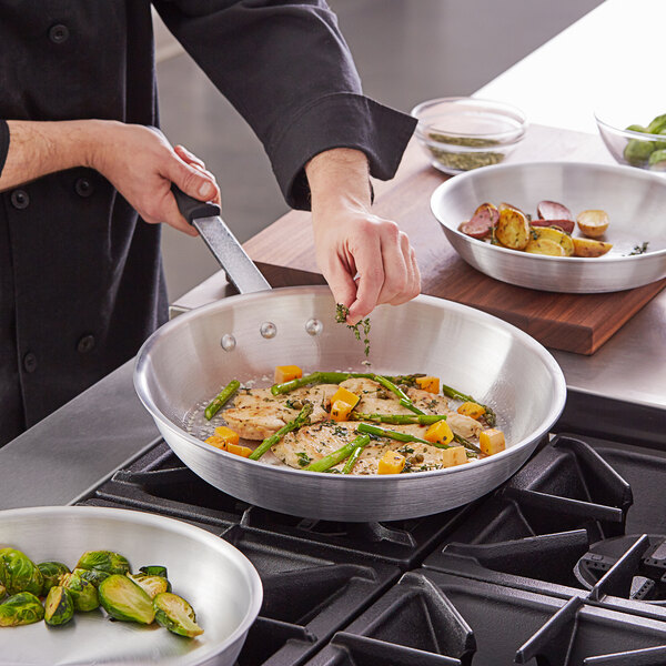 A person cooking brussels sprouts and green beans in a Vollrath Arkadia aluminum fry pan on a stove.
