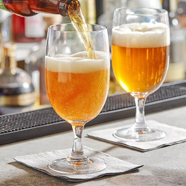 A person pouring beer into an Arcoroc beer goblet on a table in a bar.