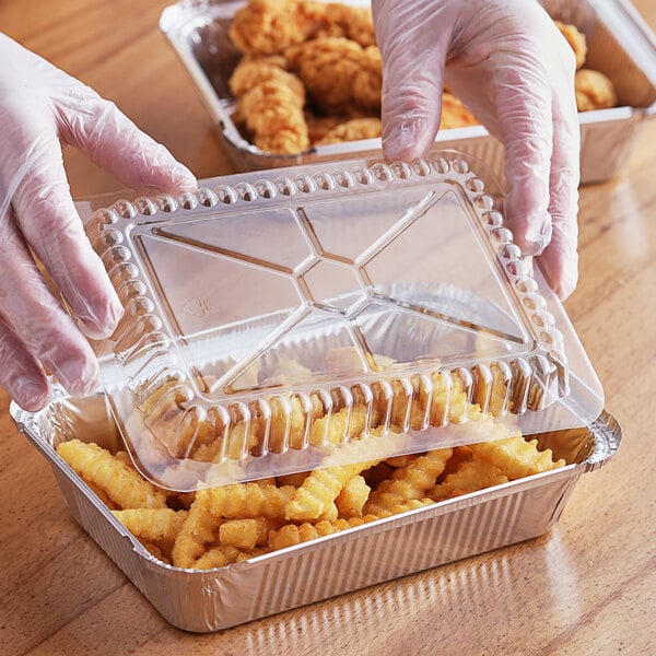 A gloved hand in plastic gloves holds a clear plastic container of food.