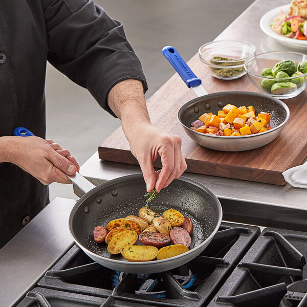 A person cooking food in a Vollrath Wear-Ever non-stick frying pan with blue handles.
