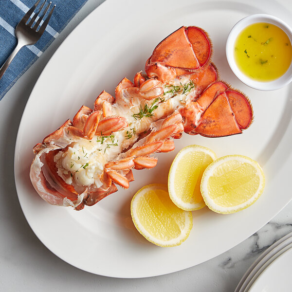 A Boston Lobster Company 12-14 oz. lobster tail on a plate with lemon slices and sauce.