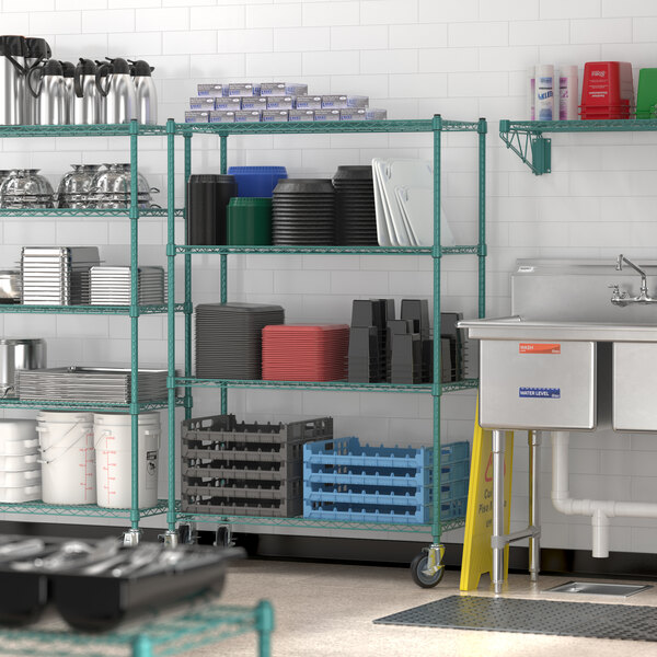 A commercial kitchen with green metal shelving units on wheels, holding various kitchen supplies and containers next to a stainless steel sink.