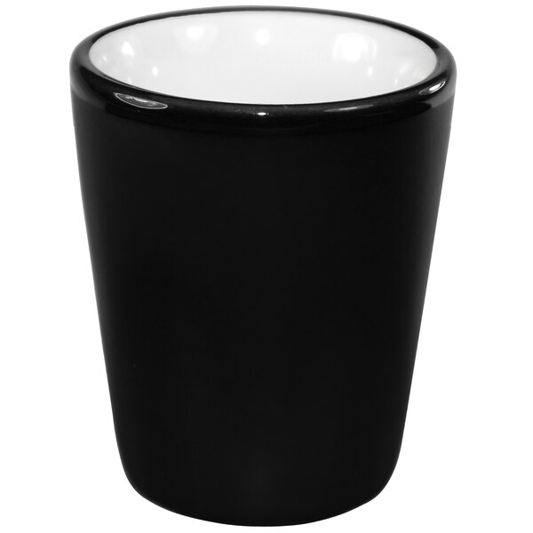 A white stoneware shot glass with a black interior and white rim.