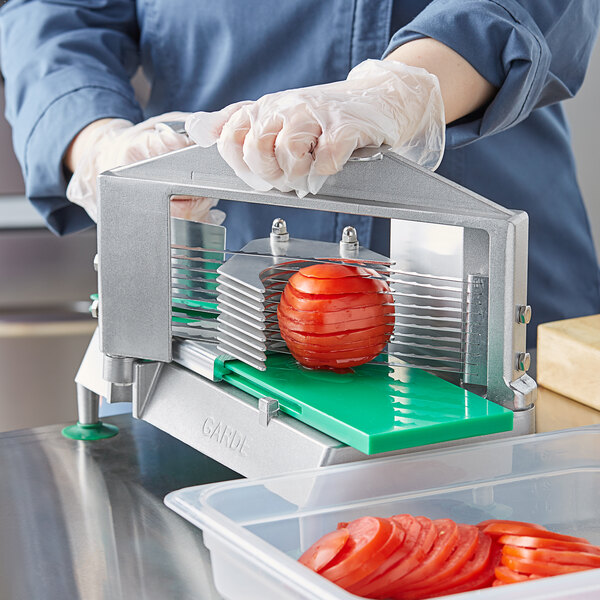 A person using a Garde XL tomato slicer to cut tomatoes on a counter.