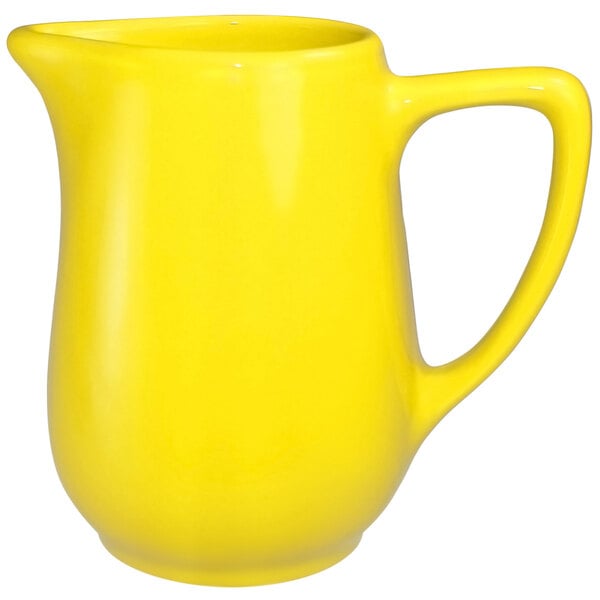 A yellow stoneware creamer with a handle.
