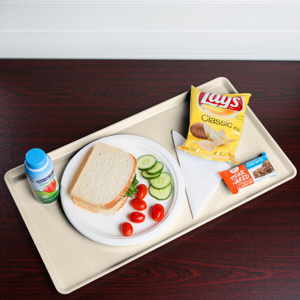 A light peach Cambro dietary tray with a sandwich, chips, and a drink on it.