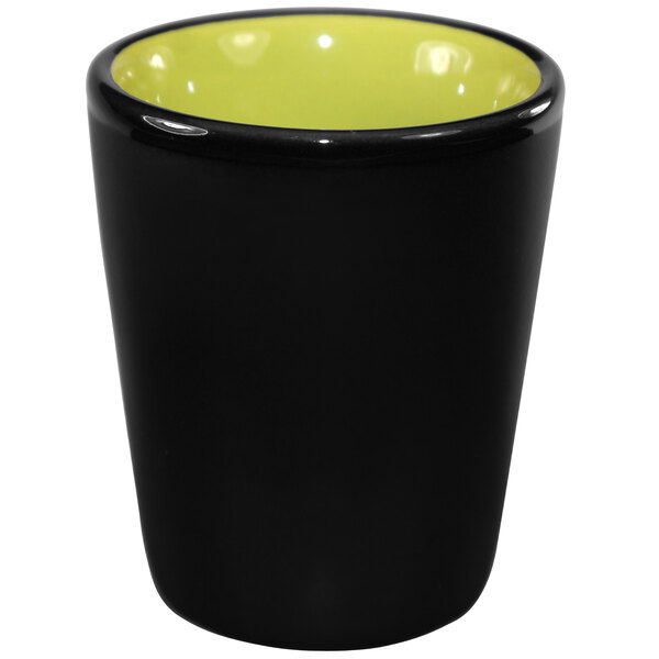 A black and lime green stoneware shot glass with a yellow interior.