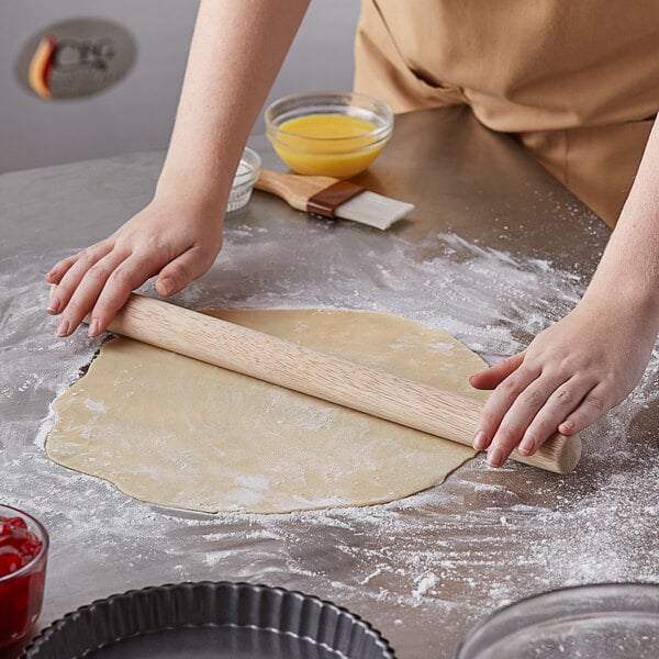 A person rolling out dough with an American Metalcraft wood French rolling pin.