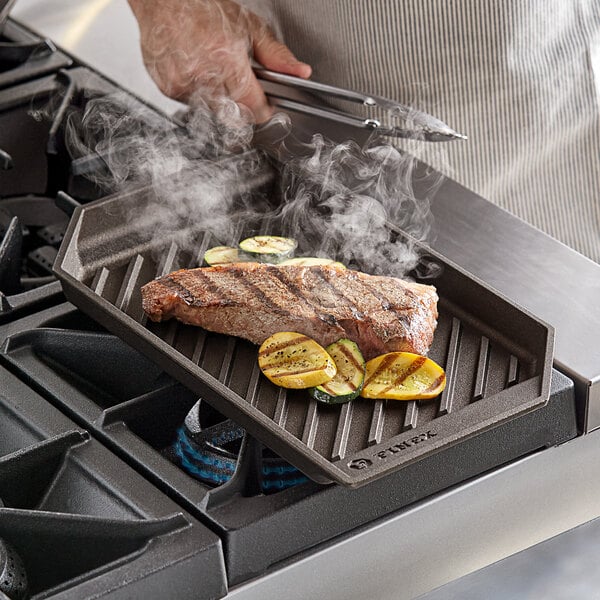 A person using a FINEX rectangle cast iron grill pan to cook a steak on a grill.