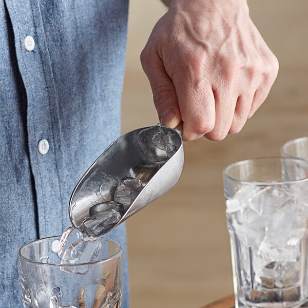 A hand using a Vollrath cast aluminum ice scoop to put ice in a glass.