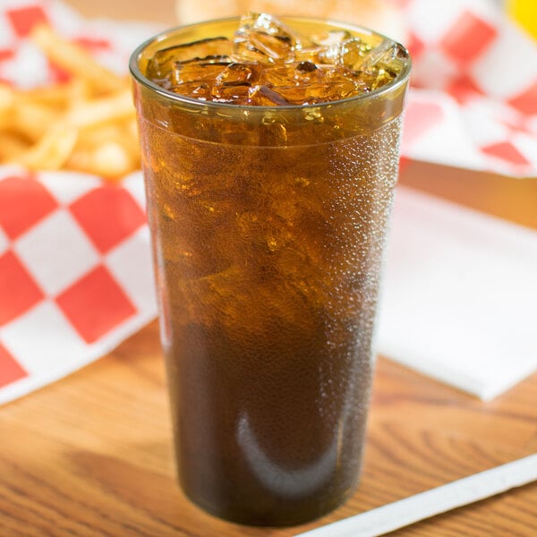 A Carlisle amber plastic tumbler filled with brown liquid and ice on a table with fries and a straw.