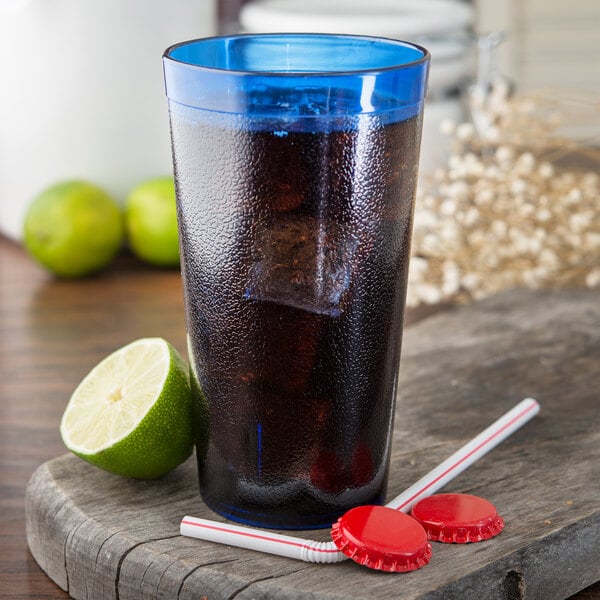 A Carlisle royal blue plastic tumbler with a drink, limes, and a straw.