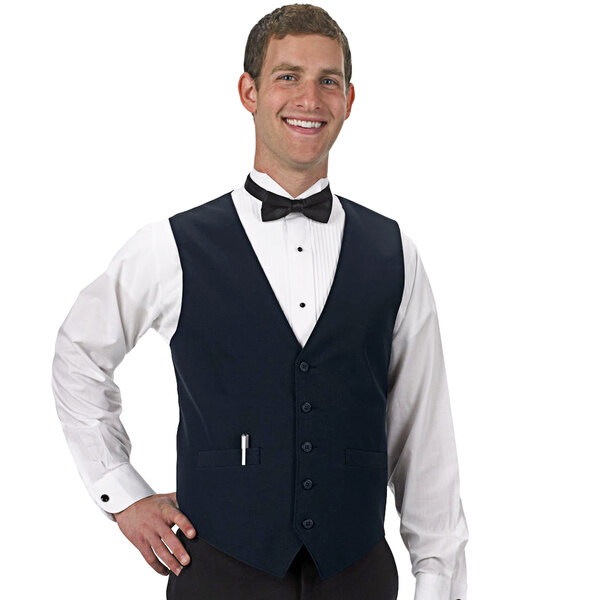 A man wearing a navy blue Henry Segal server vest and bow tie with his hands in his pockets.