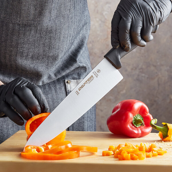 A person in gloves using a Dexter-Russell SofGrip chef knife to cut a tomato on a cutting board.