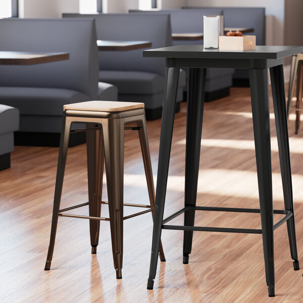 A Lancaster Table & Seating copper backless barstool with a natural wood seat at a table in a restaurant.
