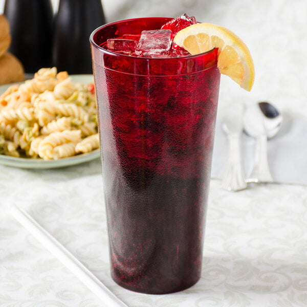 A Carlisle Ruby plastic tumbler filled with red liquid, ice, and a lemon slice.
