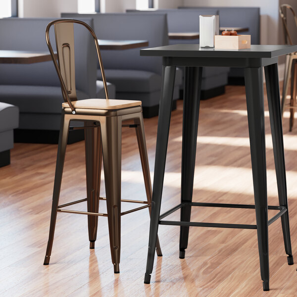 A Lancaster Table & Seating copper barstool with a natural wood seat next to a metal table.